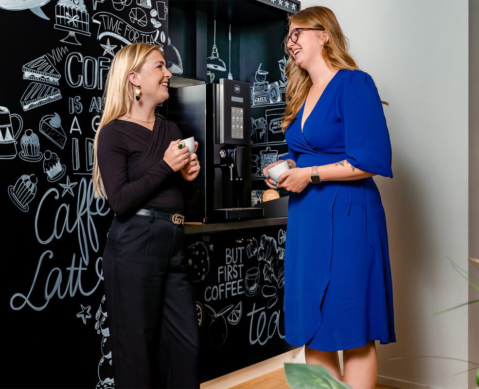 Zijaanzicht twee dames met een kop koffie in gesprek met elkaar