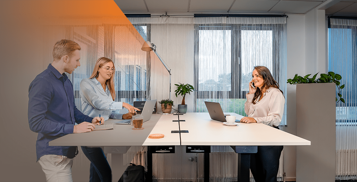 Een collega aan de telefoon, andere collega kijkt naar een laptop waar de andere collega naar wijst